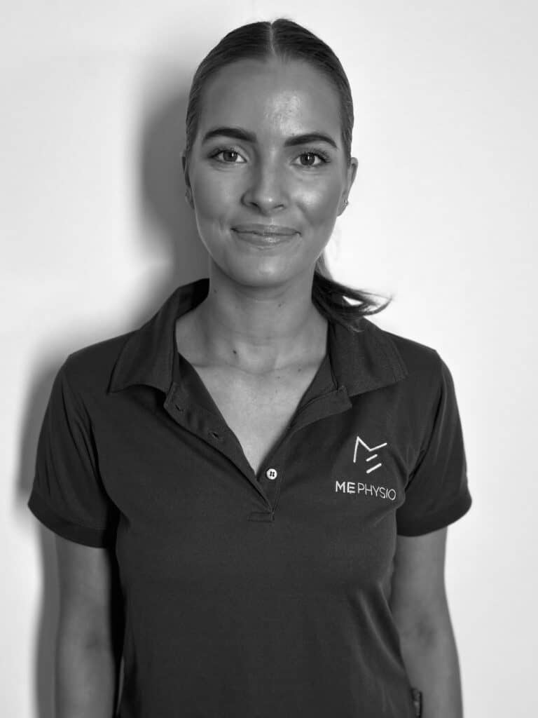 A woman with a neat ponytail and sleek hair, wearing a dark polo shirt with a small logo on the left chest that reads "ME PHYSIO." She stands against a plain white background, looking directly at the camera with a slight smile.