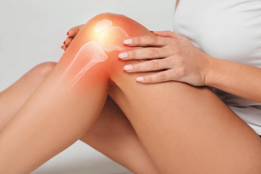 A person holds their knee, which is highlighted with a reddish glow and an illustration of the knee joint, indicating pain or discomfort—common knee symptoms that may require specialized knee treatment or attention to underlying knee conditions.