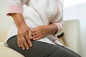 An older adult sitting on a couch, holding their hip in apparent discomfort, with a cane visible in the background—highlighting the importance of seeking hip pain relief and physio support.